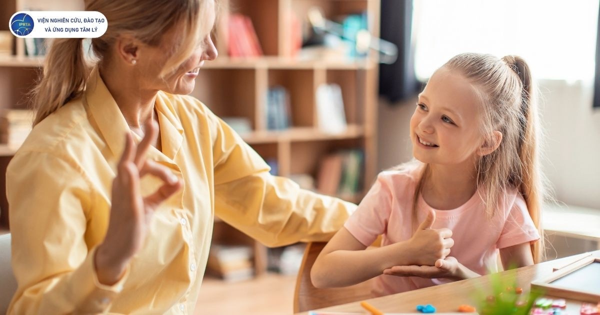 Một nhà trị liệu ngôn ngữ đang nhẹ nhàng hướng dẫn một trẻ mắc rối loạn phát triển ngôn ngữ bằng cử chỉ để hỗ trợ giao tiếp, tạo môi trường tương tác thân thiện và khuyến khích trẻ diễn đạt ý tưởng của mình.